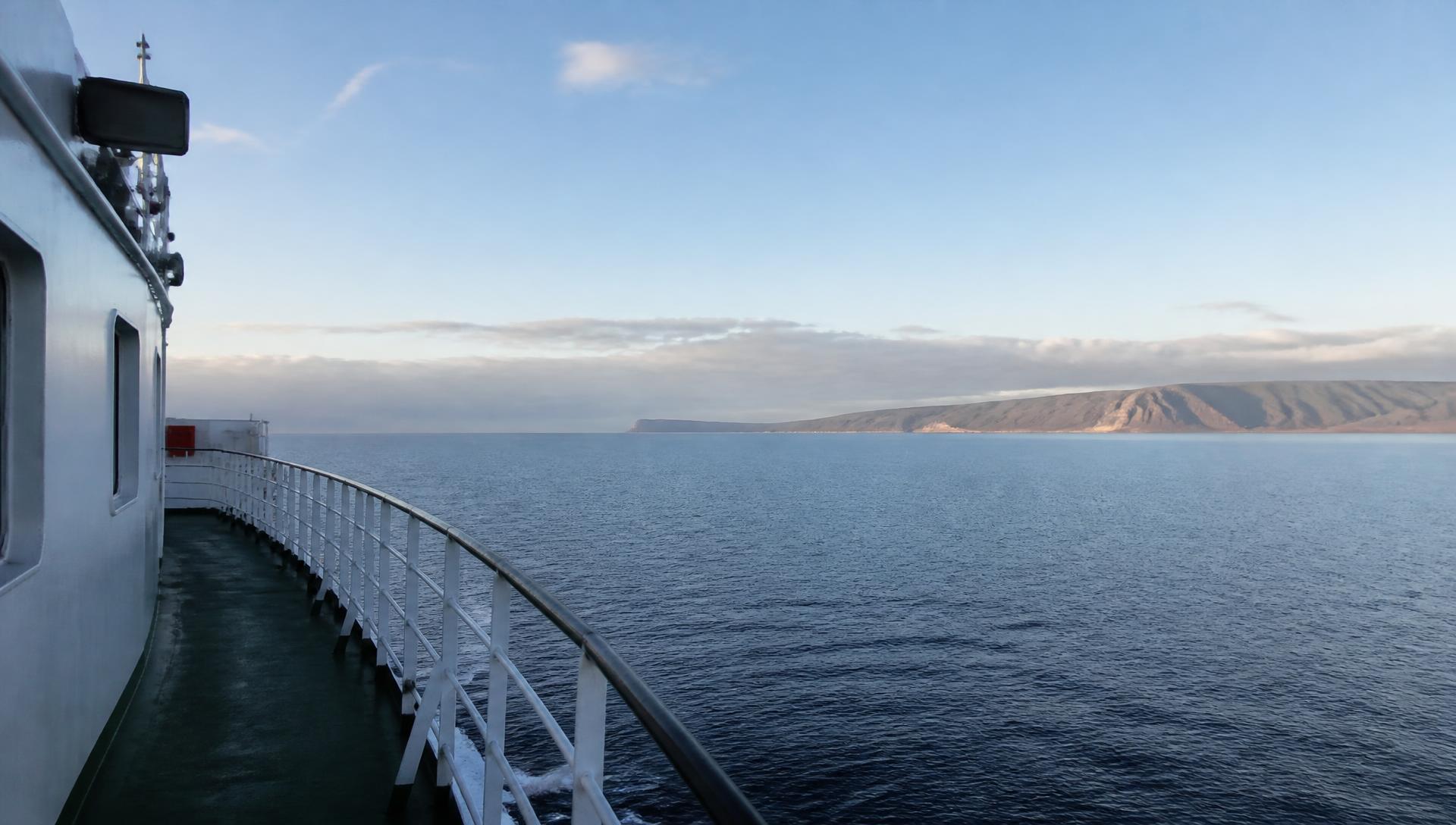 Deck de navio em mar aberto com uma costa distante no horizonte
